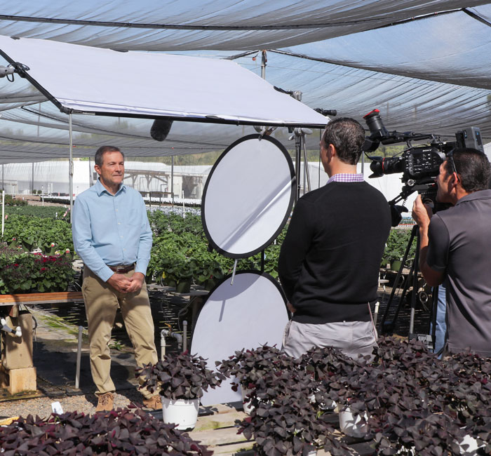 Eric Larson stands in a greenhouse and faces a film crew.